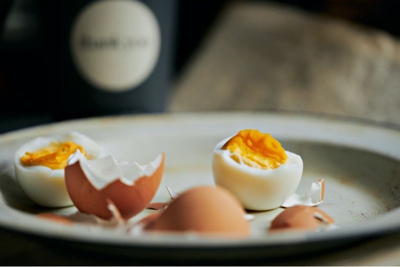 Two hard-boiled eggs on a plate that are partially eaten with their brown shells next to them.