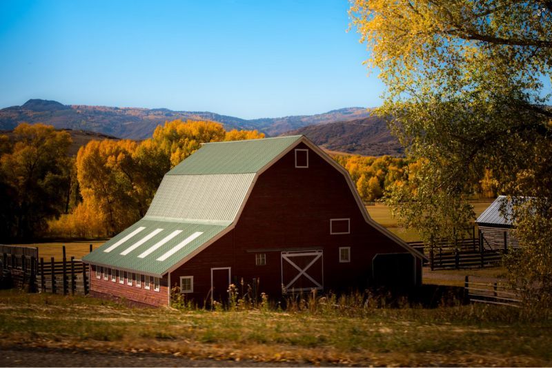 A red gambrel-roofed barn on a field on a clear day in autumn