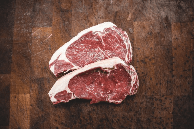 Two steaks next to each other on a wooden surface