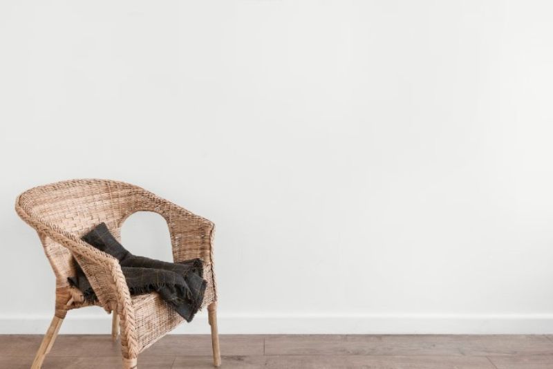 A wicker chair with a folded black blanket in a plain white room with wooden floors.
